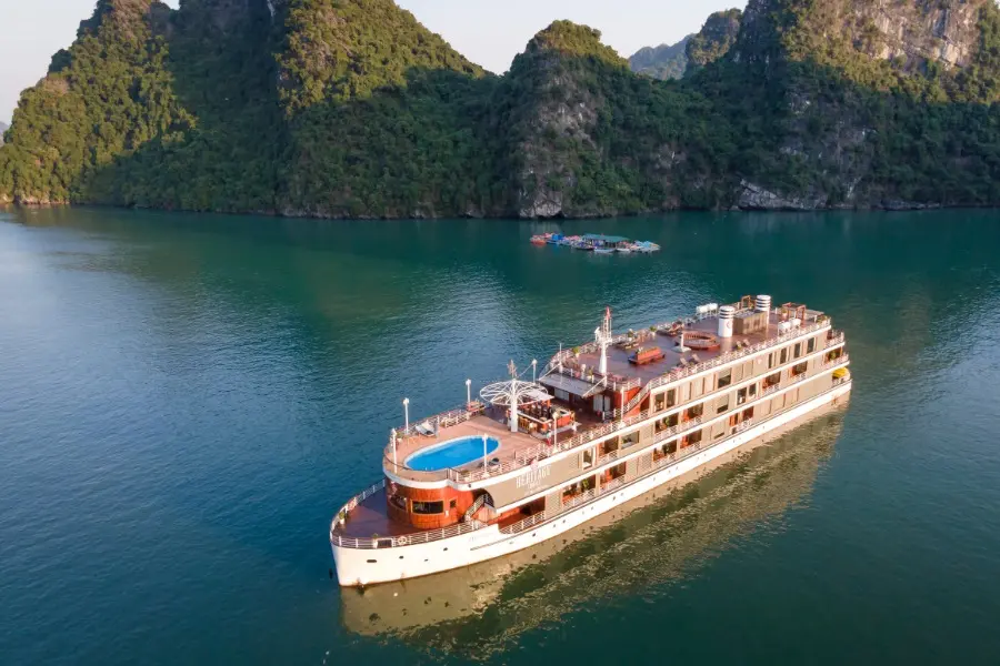 Luxury cruise ship with a pool on deck sailing through a scenic bay surrounded by lush green mountains and calm waters, perfect for a relaxing travel experience.