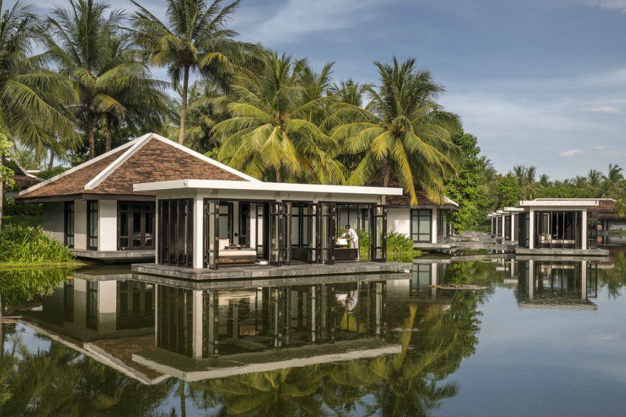 Four Seasons Nam Hai's Spa is set on tranquil water villas at a luxury beach resort in Vietnam, surrounded by lush palm trees and calm waters, reflecting the serene environment and modern architecture.