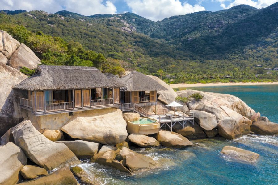 Six senses Ninh Van Bay's Rock Pool Villa, a luxury beach villa in Vietnam nestled among large rocks and lush greenery, overlooking a turquoise sea with a private hot tub and scenic mountain backdrop.