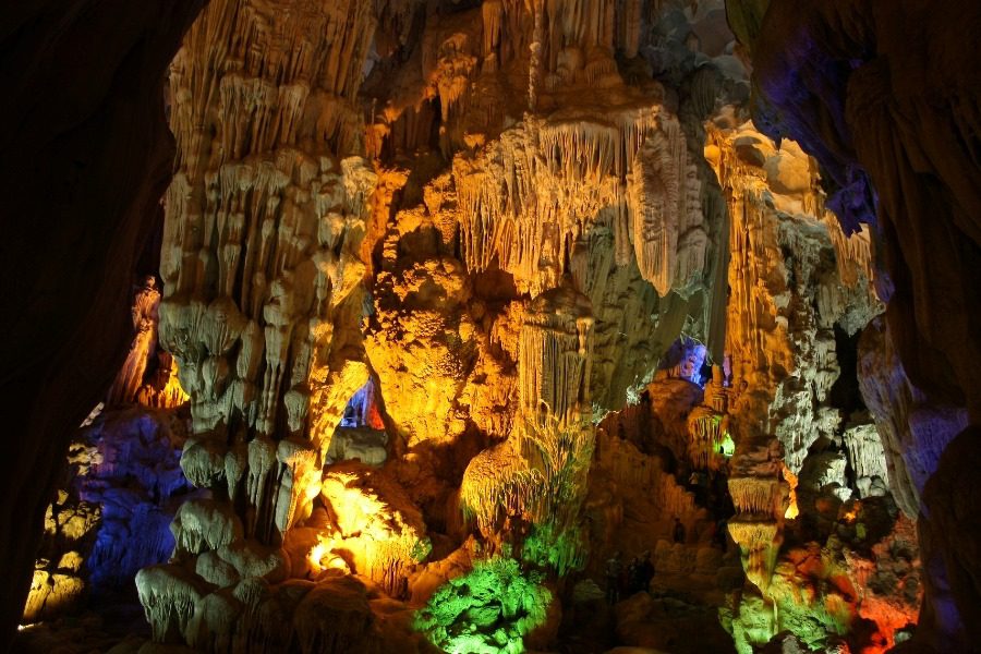 Stunning cave interior illuminated with colorful lights, showcasing intricate stalactites and stalagmites, a natural wonder perfect for adventure and nature tourism.