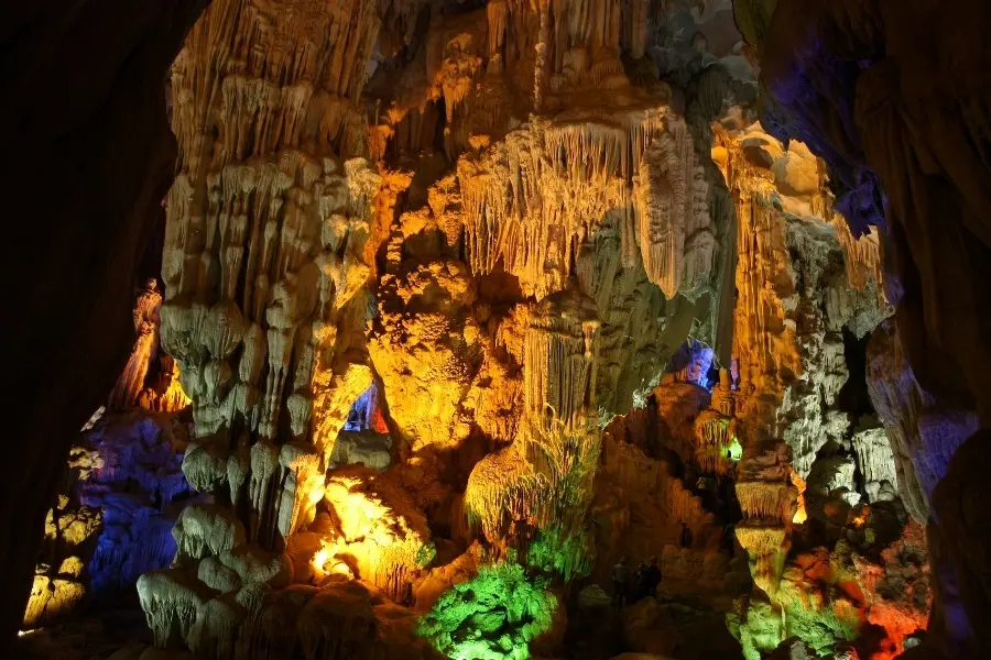 Stunning cave interior illuminated with colorful lights, showcasing intricate stalactites and stalagmites, a natural wonder perfect for adventure and nature tourism.